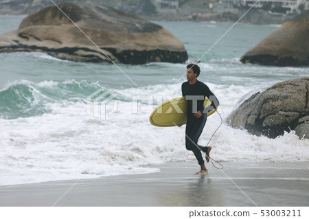 Male surfer holding surfboard while running on beach  53003211