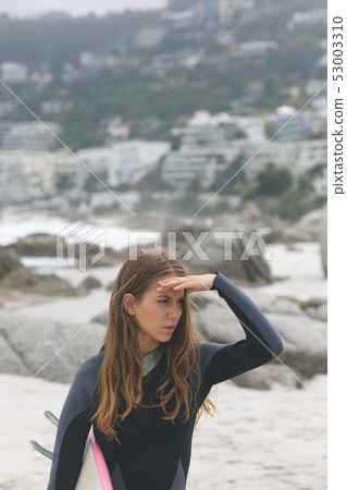 Woman standing with surfboard shielding eyes at beach 53003310
