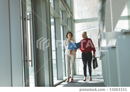 Businesswomen discussing over document while walking in office building 53003331