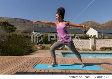 Woman performing stretching exercise in the backyard of home Woman performing stretching exercise in the backyard of home 53003472