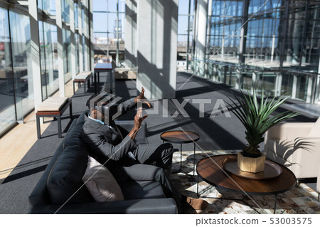 African-American businessman sitting on the sofa and using virtual reality headset in office African-American businessman sitting on the sofa and using virtual reality headset in office 53003575