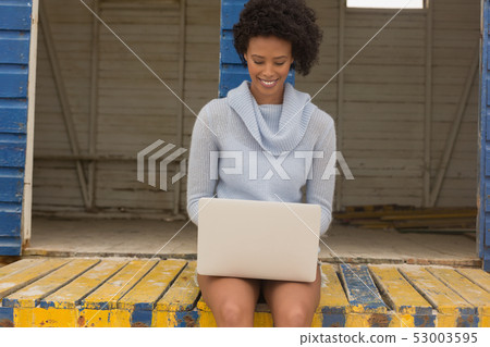 Young African American woman using laptop at beach hut Young African American woman using laptop at beach hut 53003595