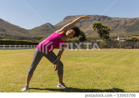 Woman performing stretching exercise in the backyard of home Woman performing stretching exercise in the backyard of home 53003706
