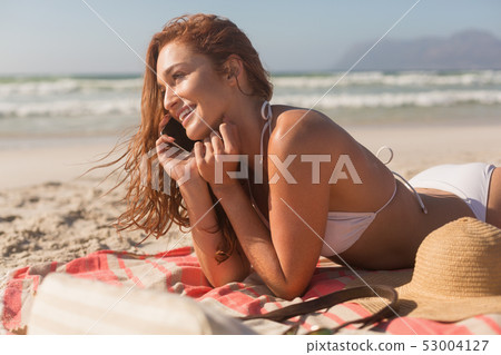 Young Caucasian woman in bikini lying on the sand and talking to mobile phone Young Caucasian woman in bikini lying on the sand and talking to mobile phone 53004127