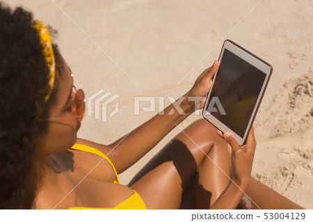 Young African American woman in yellow bikini and sunglasses using digital tablet Young African American woman in yellow bikini and sunglasses using digital tablet 53004129