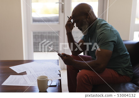 Senior man filling form while using digital tablet in living room Senior man filling form while using digital tablet in living room 53004132