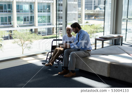 Disabled mixed-race female executive with Caucasian businessman discussing over digital tablet in th Disabled mixed-race female executive with Caucasian businessman discussing over digital tablet in th 53004133
