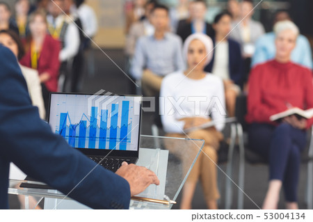 Businessman using graphs while he speaks at a business seminar Businessman using graphs while he speaks at a business seminar 53004134