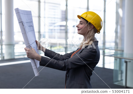Blonde Caucasian female architect looking at blueprint in modern office Blonde Caucasian female architect looking at blueprint in modern office 53004171