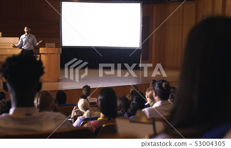 Businessman standing and giving presentation in auditorium Businessman standing and giving presentation in auditorium 53004305