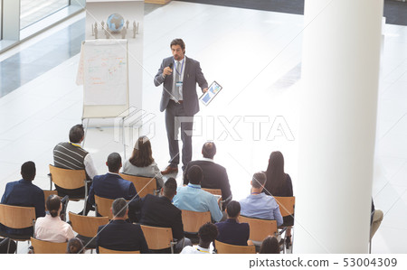 Businessman speaking at conference while holding digital tablet and microphone at business seminar 53004309
