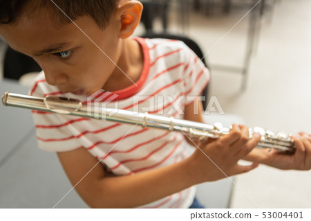 Schoolboy playing flute in a classroom 53004401
