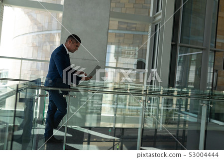 Side view of a handsome businessman working on his laptop on the first floor walkway of the office Side view of a handsome businessman working on his laptop on the first floor walkway of the office 53004444