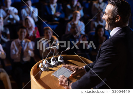 Businessman standing and giving presentation in the auditorium Businessman standing and giving presentation in the auditorium 53004449