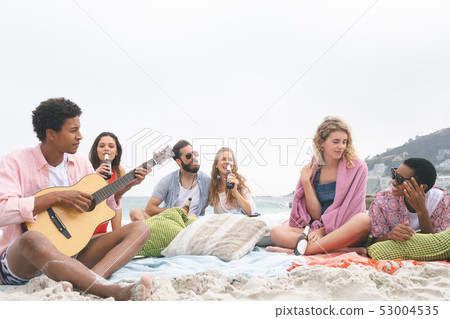Man playing guitar while friends enjoying on beach Man playing guitar while friends enjoying on beach 53004535