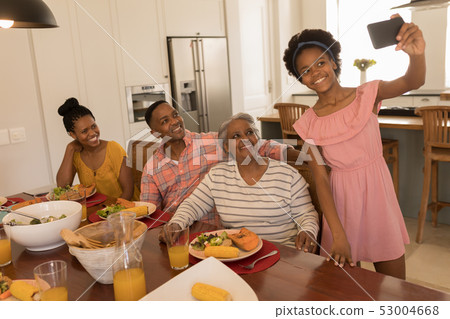 Girl taking selfie of family with mobile phone on dining table at home 53004668