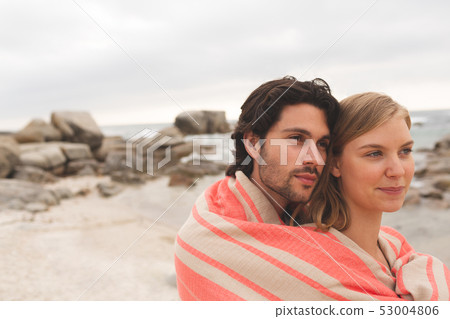 Caucasin couple wrapped in blanket standing at beach Caucasin couple wrapped in blanket standing at beach 53004806