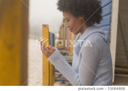Young African American woman using mobile phone at beach hut Young African American woman using mobile phone at beach hut 53004808