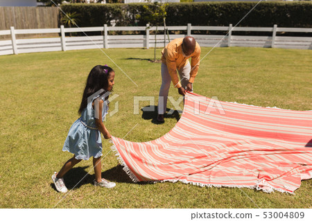 Grandfather and granddaughter placing picnic blanket in the backyard 53004809
