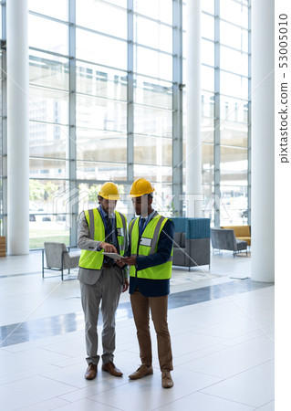 Multi-ethnic business architect standing and discussing over the digital tablet in lobby at office Multi-ethnic business architect standing and discussing over the digital tablet in lobby at office 53005010