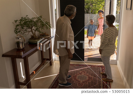 Grandparents standing near door and inviting their grandchildren in home 53005015