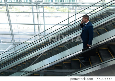 Businessman talking on mobile phone while moving down on escalator Businessman talking on mobile phone while moving down on escalator 53005332