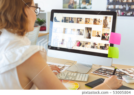 Female graphic designer working on graphic tablet at desk in office Female graphic designer working on graphic tablet at desk in office 53005804