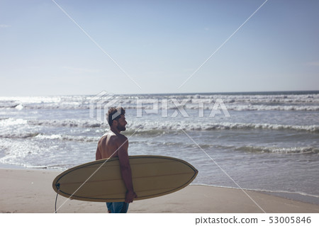 Male surfer with a surfboard standing on a beach Male surfer with a surfboard standing on a beach 53005846