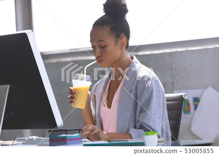 Businesswoman having milkshake while working on computer at desk 53005855