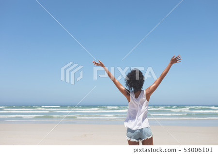 Beautiful woman standing with open arm at beach on sunny day 53006101
