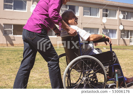 Senior woman pushing senior man on wheelchair at nursing park Senior woman pushing senior man on wheelchair at nursing park 53006176