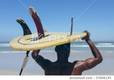 Male surfer carrying surf board at beach 53006195