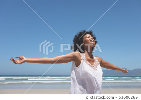 Beautiful woman standing with open arm at beach on sunny day 53006269