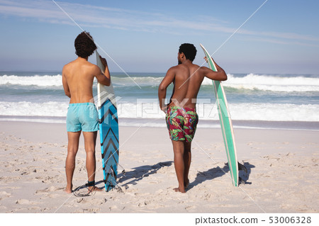 Young men with surfboard standing at beach in the sunshine 53006328