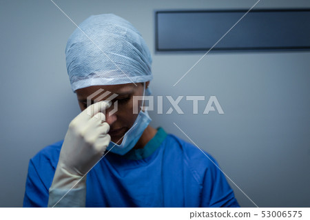 Upset female surgeon standing while leaning against the operating room door Upset female surgeon standing while leaning against the operating room door 53006575