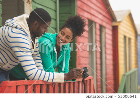 Couple using digital camera while standing at beach hut Couple using digital camera while standing at beach hut 53006641