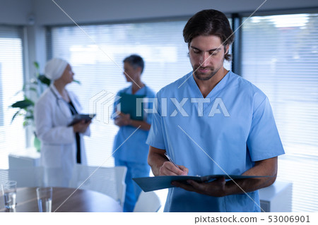 Confident male surgeon writing in medical report in clinic at hospital Confident male surgeon writing in medical report in clinic at hospital 53006901