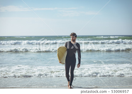 Male surfer with a surfboard walking on a beach 53006957