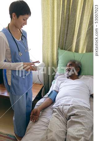 Female nurse checking blood pressure of senior male patient 53007023