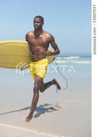 Male surfer with a surfboard running on a beach 53007037