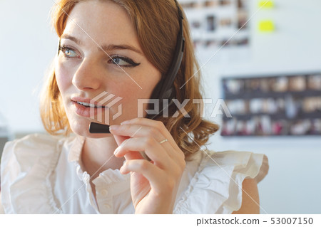Female graphic designer talking on headphone in office Female graphic designer talking on headphone in office 53007150