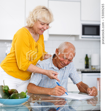 Smiling mature couple in home kitchen filling up documents 53009265