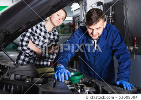 Two masters are replacing the oil in the car in workshop. 53009394