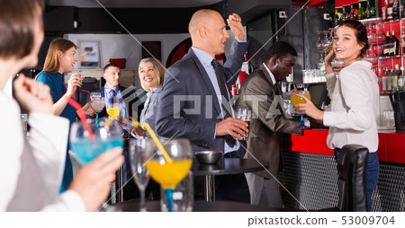 Cheerful male and female colleagues having fun on corporate party in bar Cheerful male and female colleagues having fun on corporate party in bar 53009704