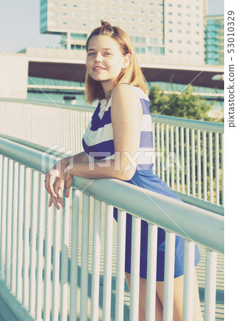 Girl in blue dress standing on city bridge Girl in blue dress standing on city bridge 53010329