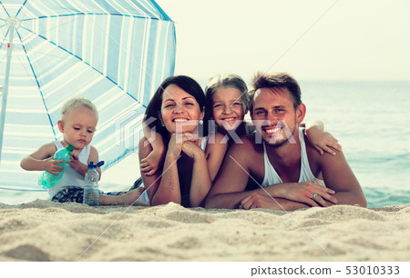parents with two kids lying on the beach. 53010333