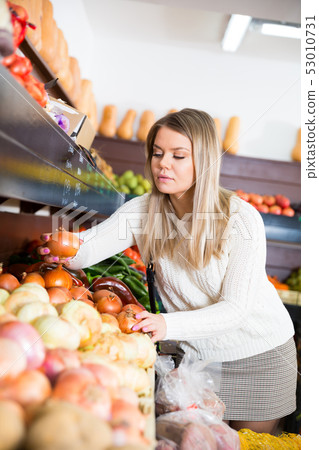 Woman choosing vegetables in greengrocery Woman choosing vegetables in greengrocery 53010731