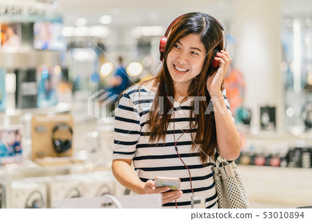 Happy Asian woman listening and testing technology Earphone or headphones in store shop or department store Happy Asian woman listening and testing technology Earphone or headphones in store shop or department store 53010894
