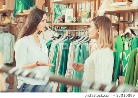 Two young women friends talking in clothes shop and smiling 53010899