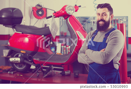 positive man worker displaying his workplace in motorcycle workshop 53010993